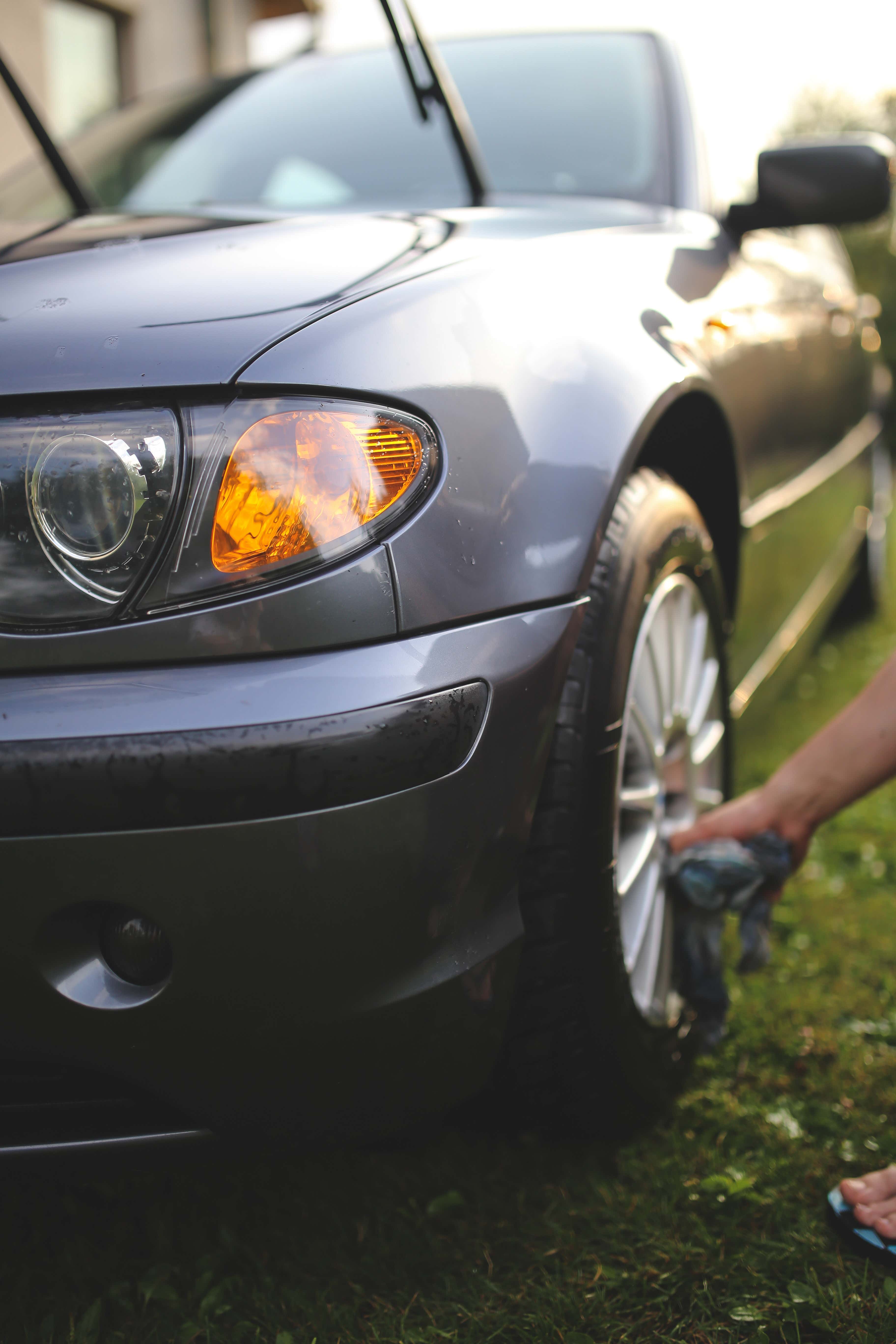A person cleaning the tires of a grey car in the morning 一个人在早上清洗一辆灰色汽车的轮胎