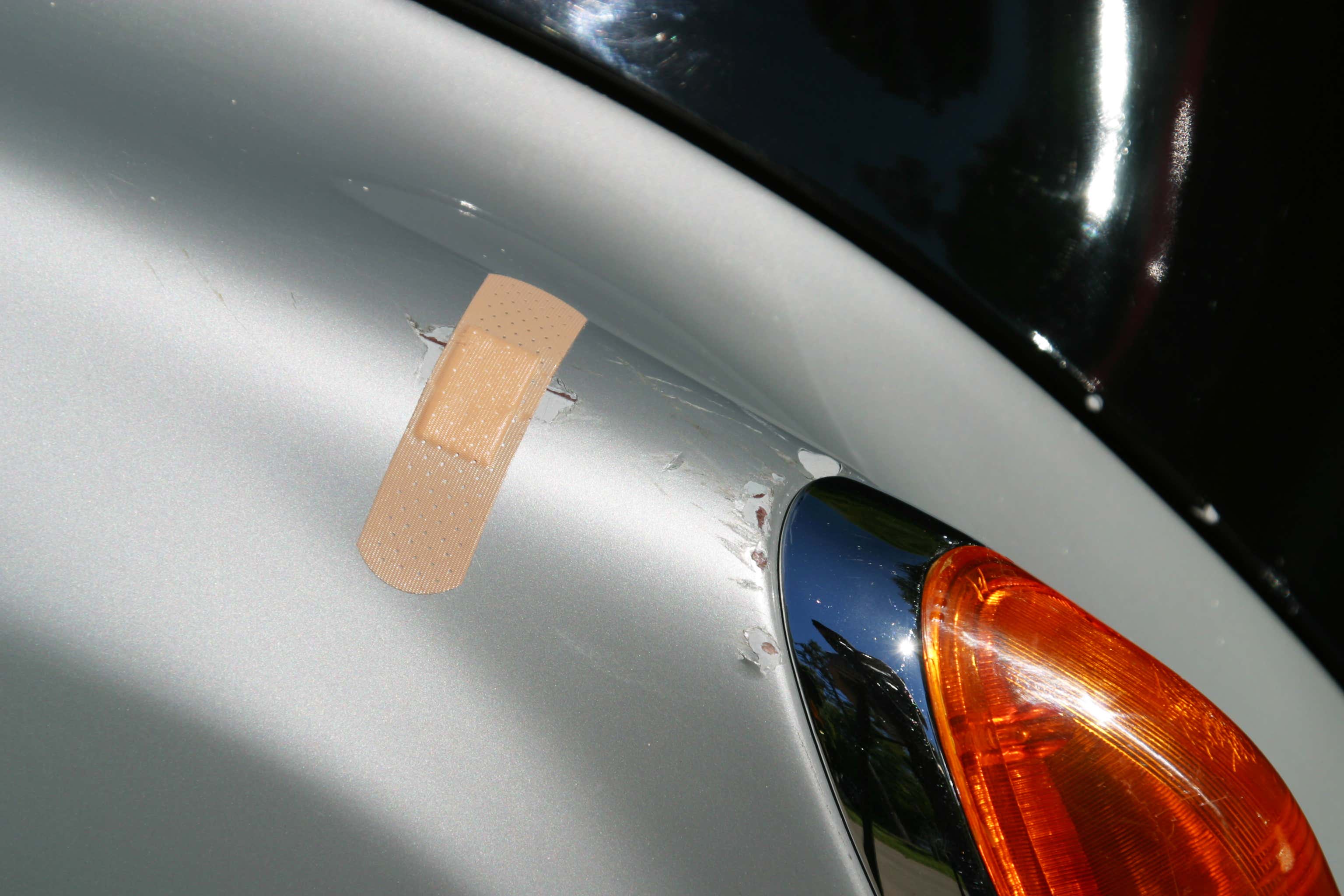 Band-Aid being used to cover a scratch on side of a silver car 一辆银色汽车边上的划痕被用创可贴覆盖