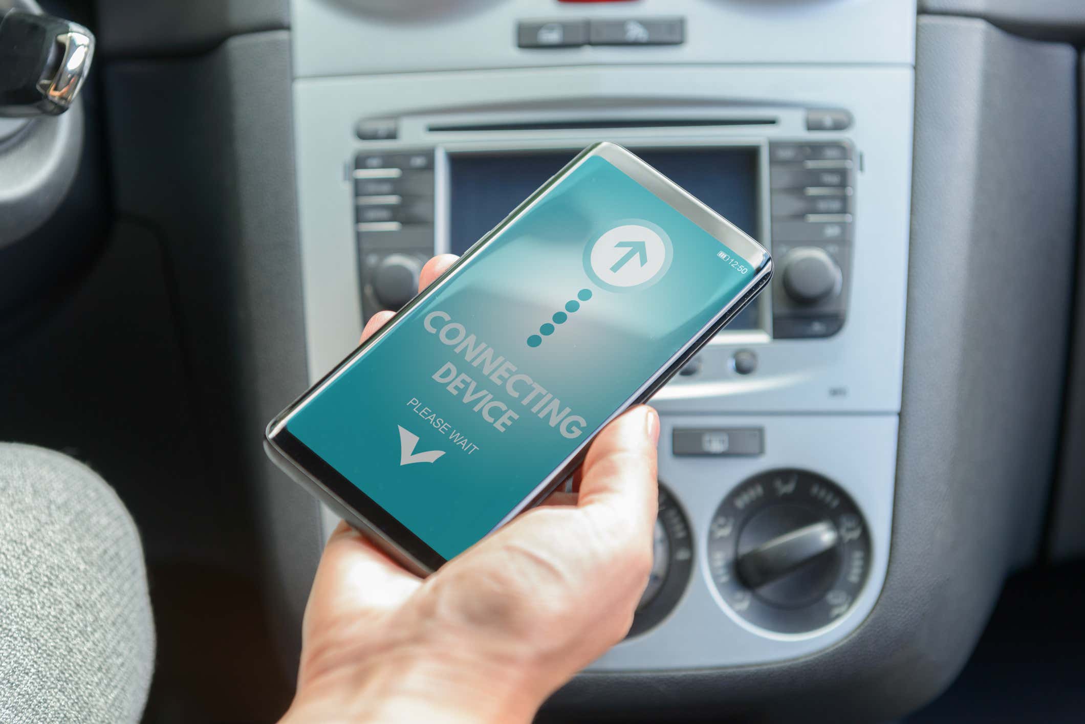 A hand holding a smartphone connecting to the car. 拿着智能手机的手连接到汽车。