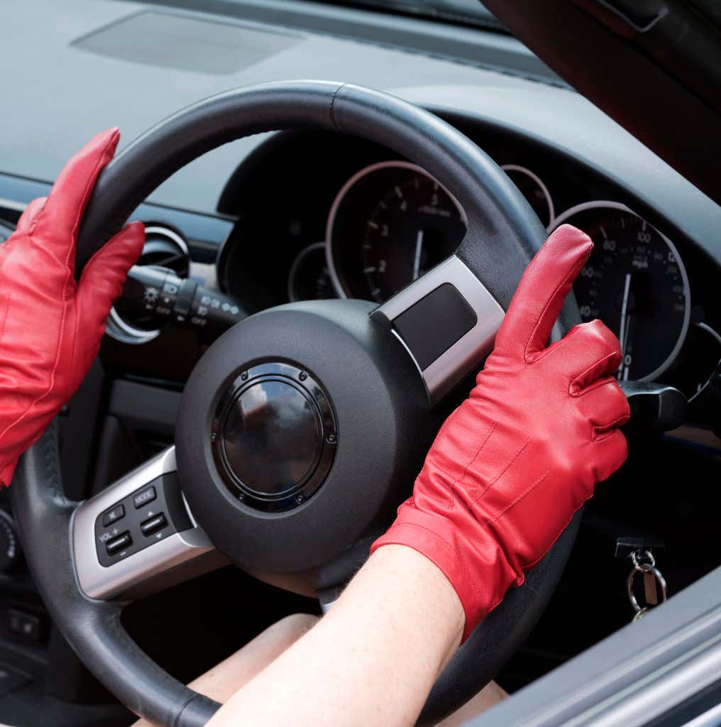 Red leather driving gloves placed on a steering wheel. 放在方向盘上的红色皮革驾驶手套。