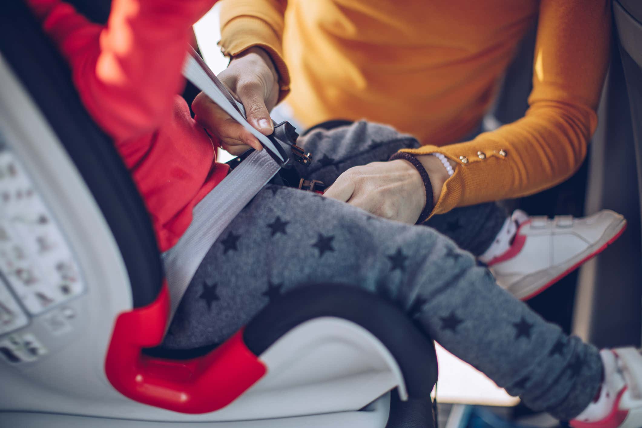 A parent secures a child into a car seat. 一位家长确保孩子到汽车座椅。