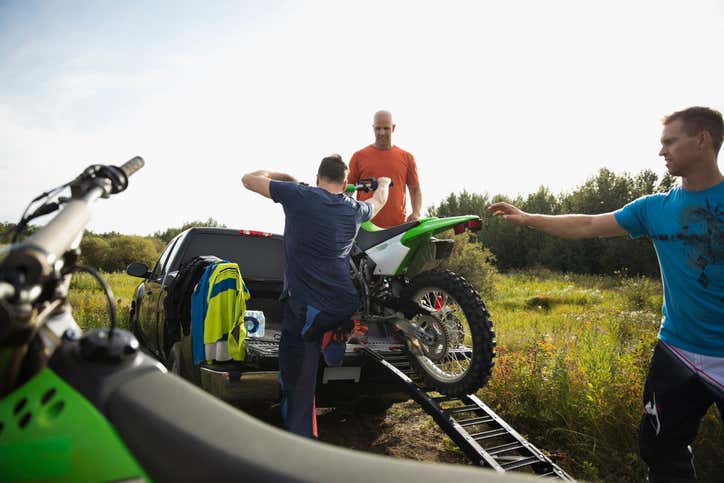 People loading a dirt bike into a truck with a ramp. 人们把越野车装进有斜坡的卡车里。