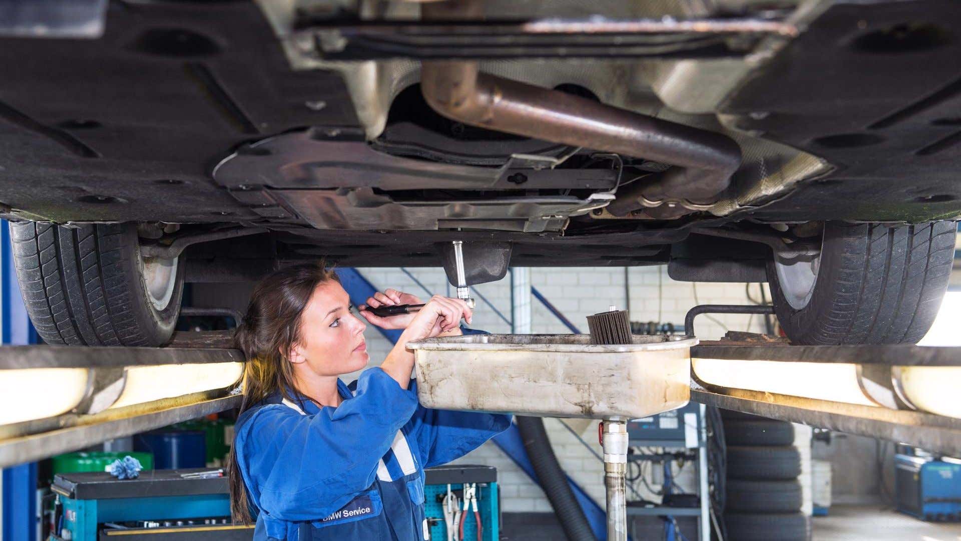 A female mechanic changes a car's oil. 一位女机械师在给汽车换机油。