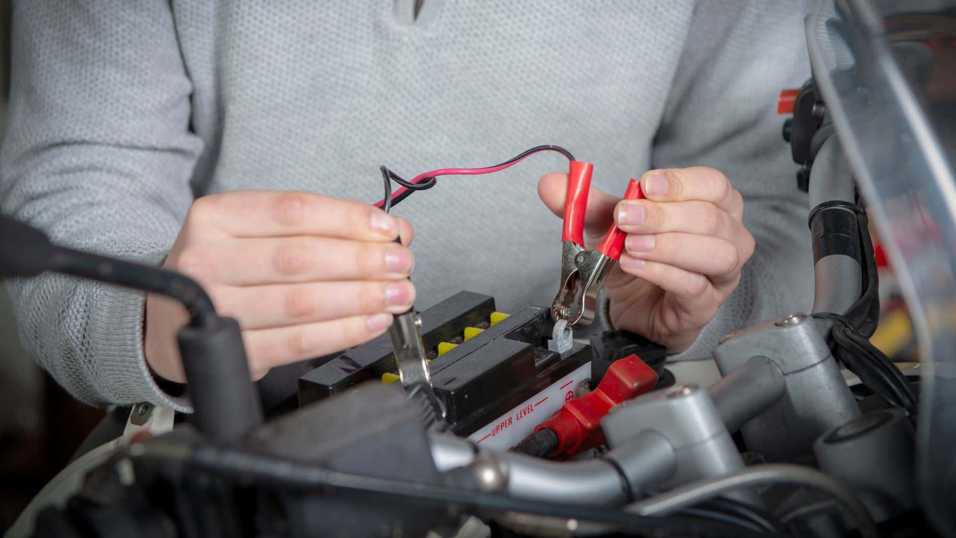 A man attaching charge cables to a motorcycle battery. 一名男子正在给摩托车电池连接充电电缆。