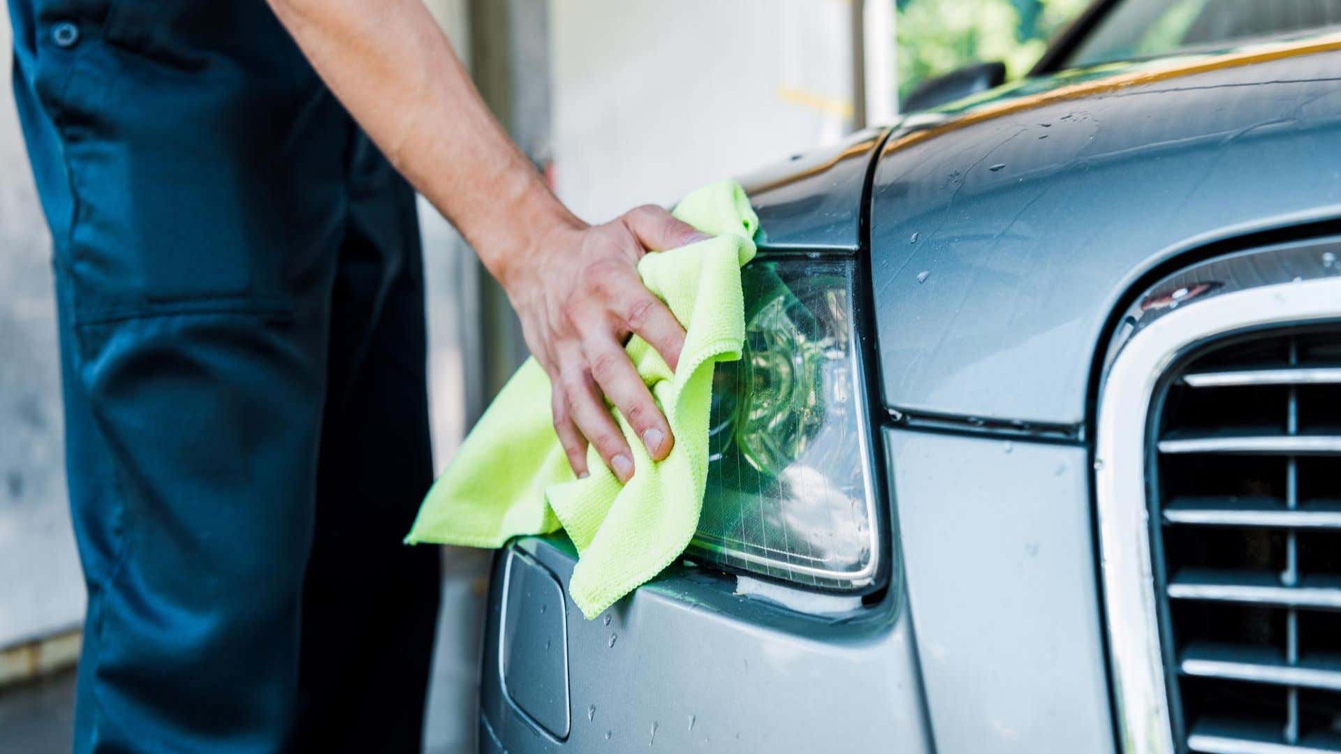 A man wiping away water on a headlight. 一名男子正在擦拭前照灯上的水。
