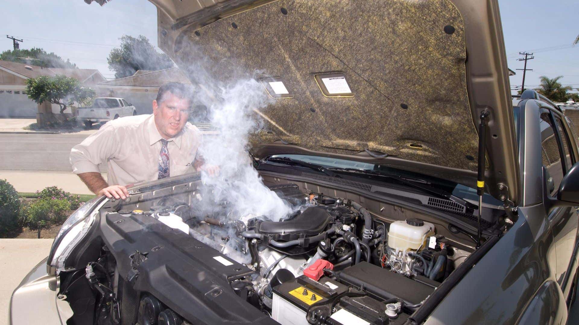 A car's engine smokes as a man looks to camera. 汽车的发动机吸烟,因为一个人看起来很镜头。