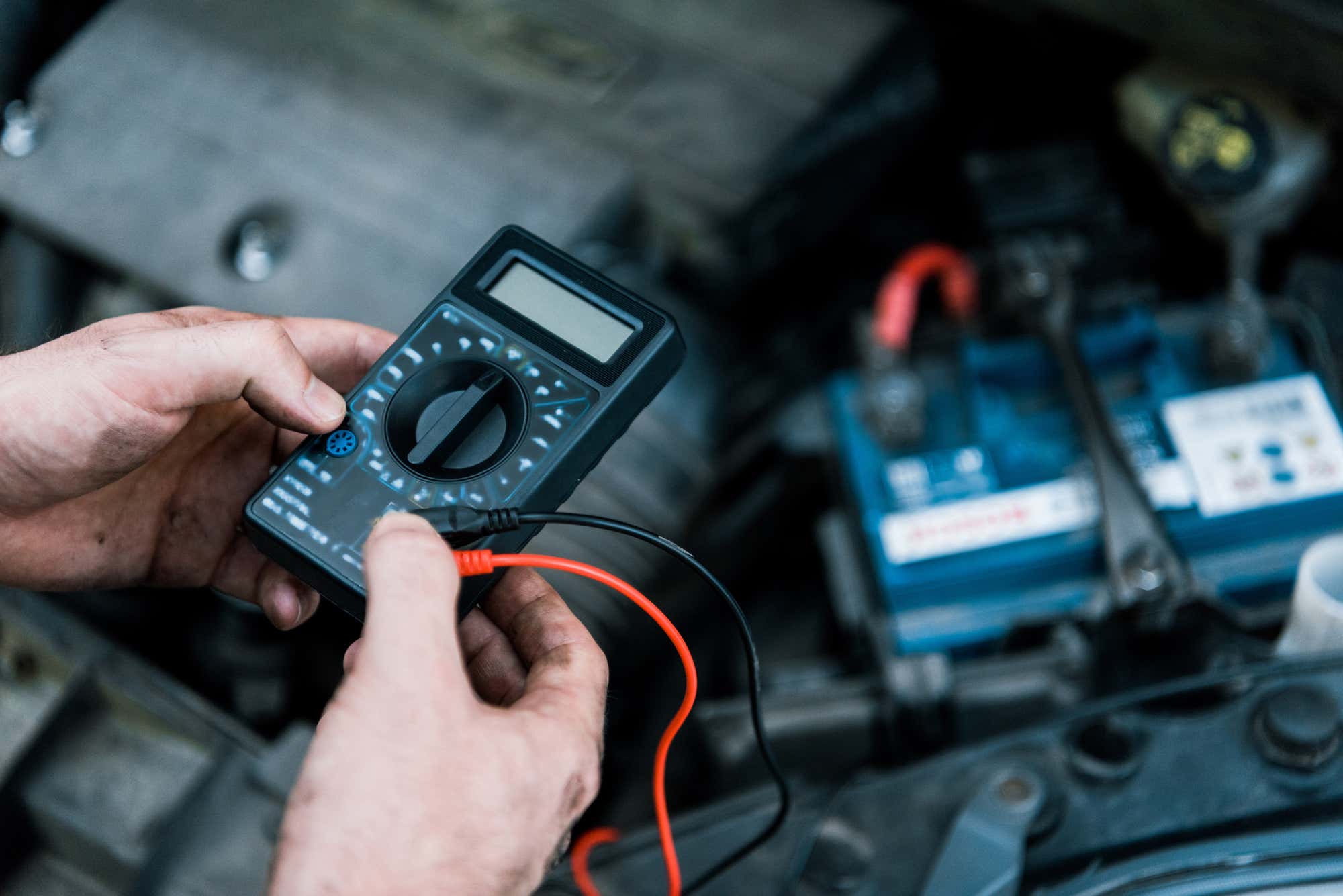 A mechanic testing a battery with a multimeter. 用万用表测试电池的技工。