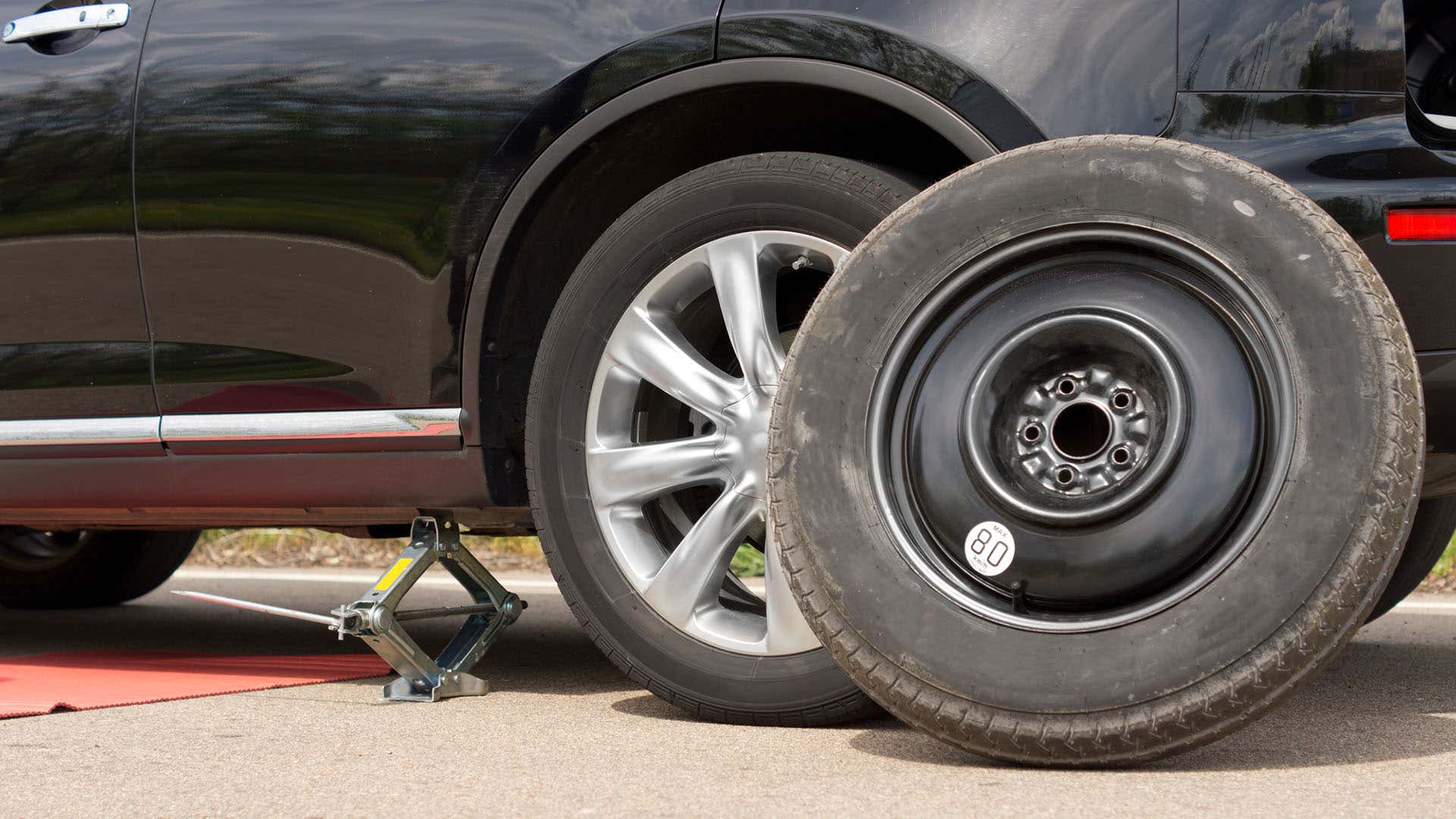 A flat tire placed next to a jacked-up car. 一个扁平的轮胎放在封闭的车旁边。