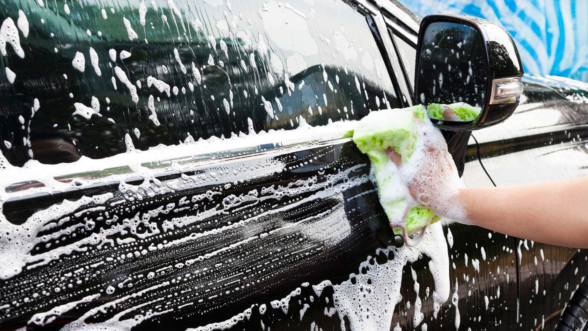 A hand using a sponge to wipe a soapy car door. 使用海绵的手擦拭肥皂车门。