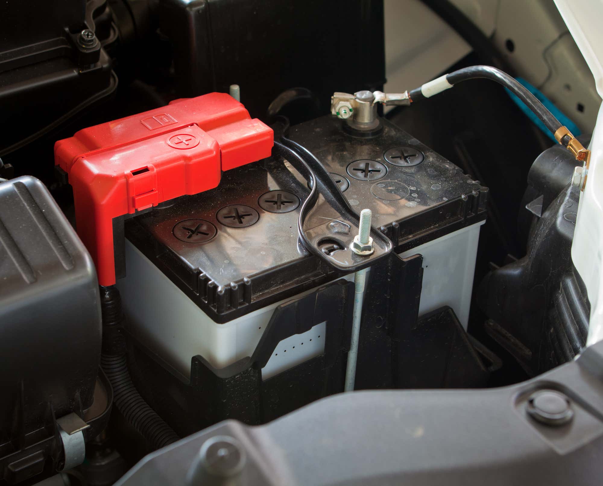 A car battery is shown with a red positive terminal cap. 汽车电池显示一个红色的正极端子帽。