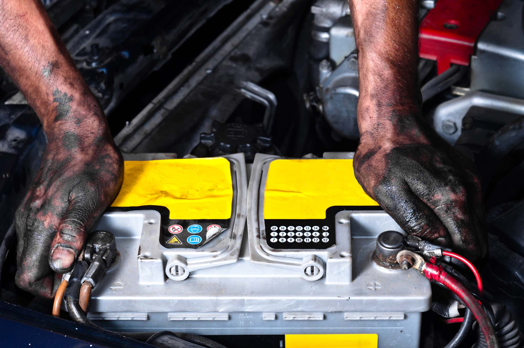 Dirty hands grip a battery in the engine bay. 肮脏的手抓住发动机湾的电池。