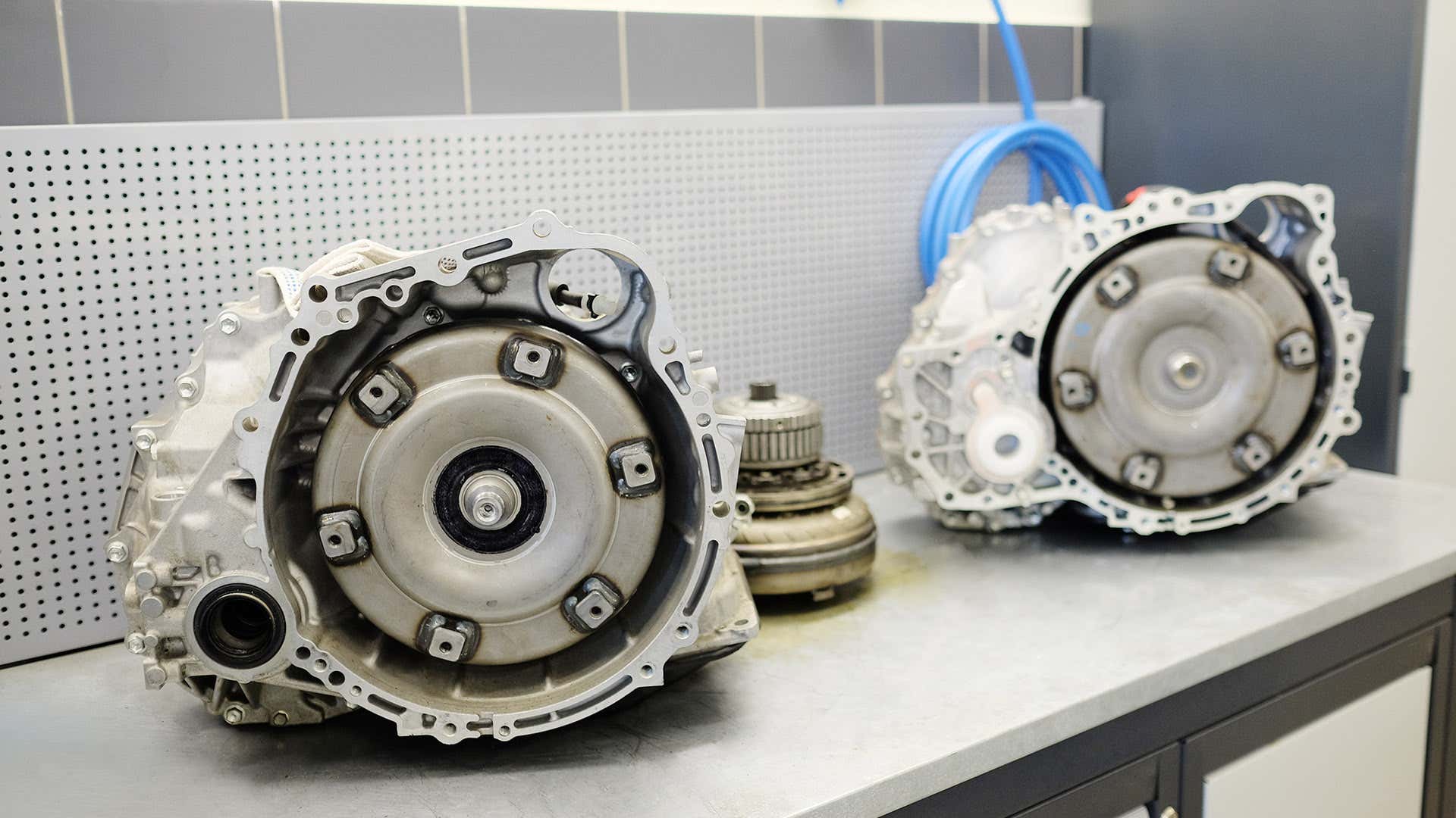 Two automatic transmissions and a torque converter sit on top of a table. 两个自动变速器和变矩器坐在桌子的顶部。