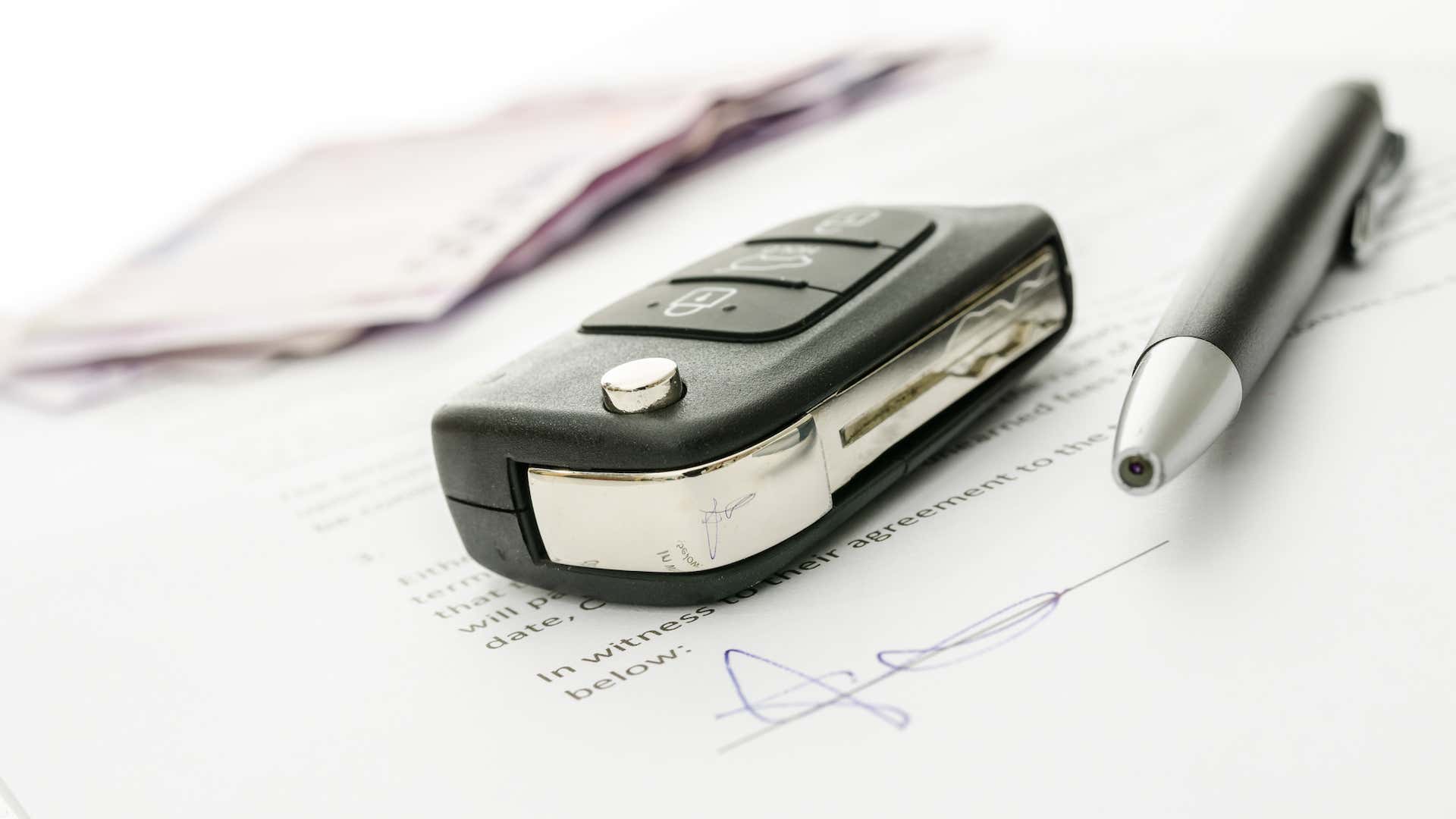 A key and pen sit on top of signed paperwork. 签过字的文件上面放着一把钥匙和一支笔。
