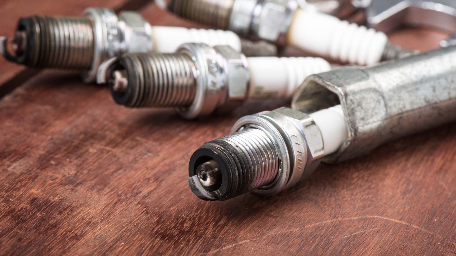 Bad spark plugs sit on a wooden table. 坏火花塞坐在一张木桌上。
