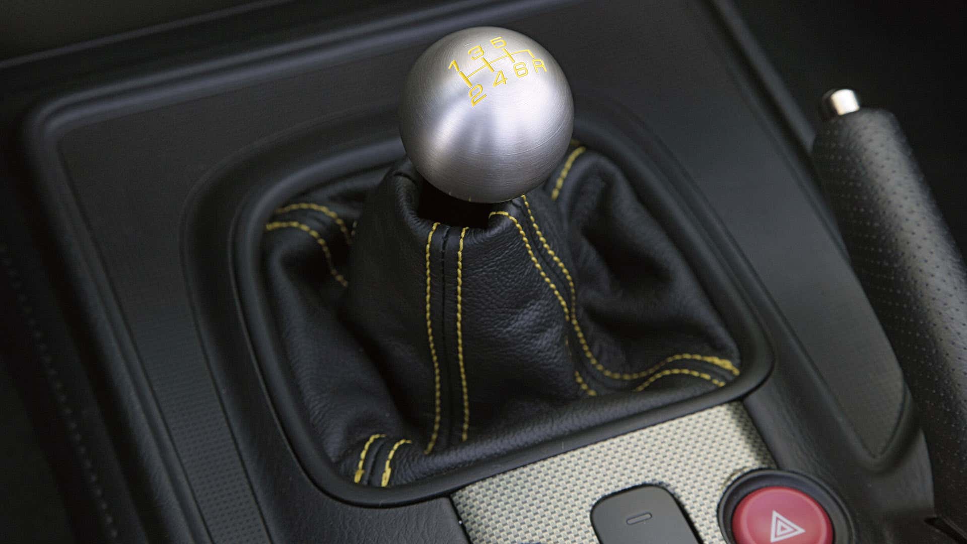 A metal ball shifter sits atop a black shift boot with yellow contrast stitching. 一个金属球移位器坐在黑色的移动靴子与黄色的对比缝纫。