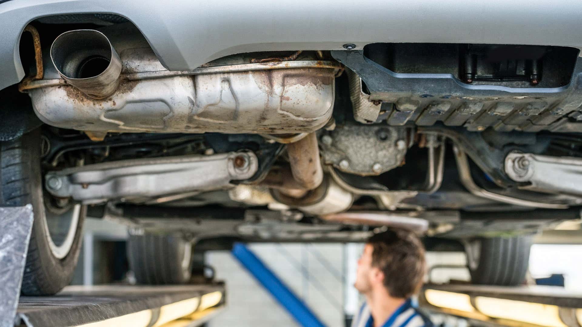 A mechanic looks at the underside of a car on a lift. 一名机械师在电梯上看着一辆汽车的底部。