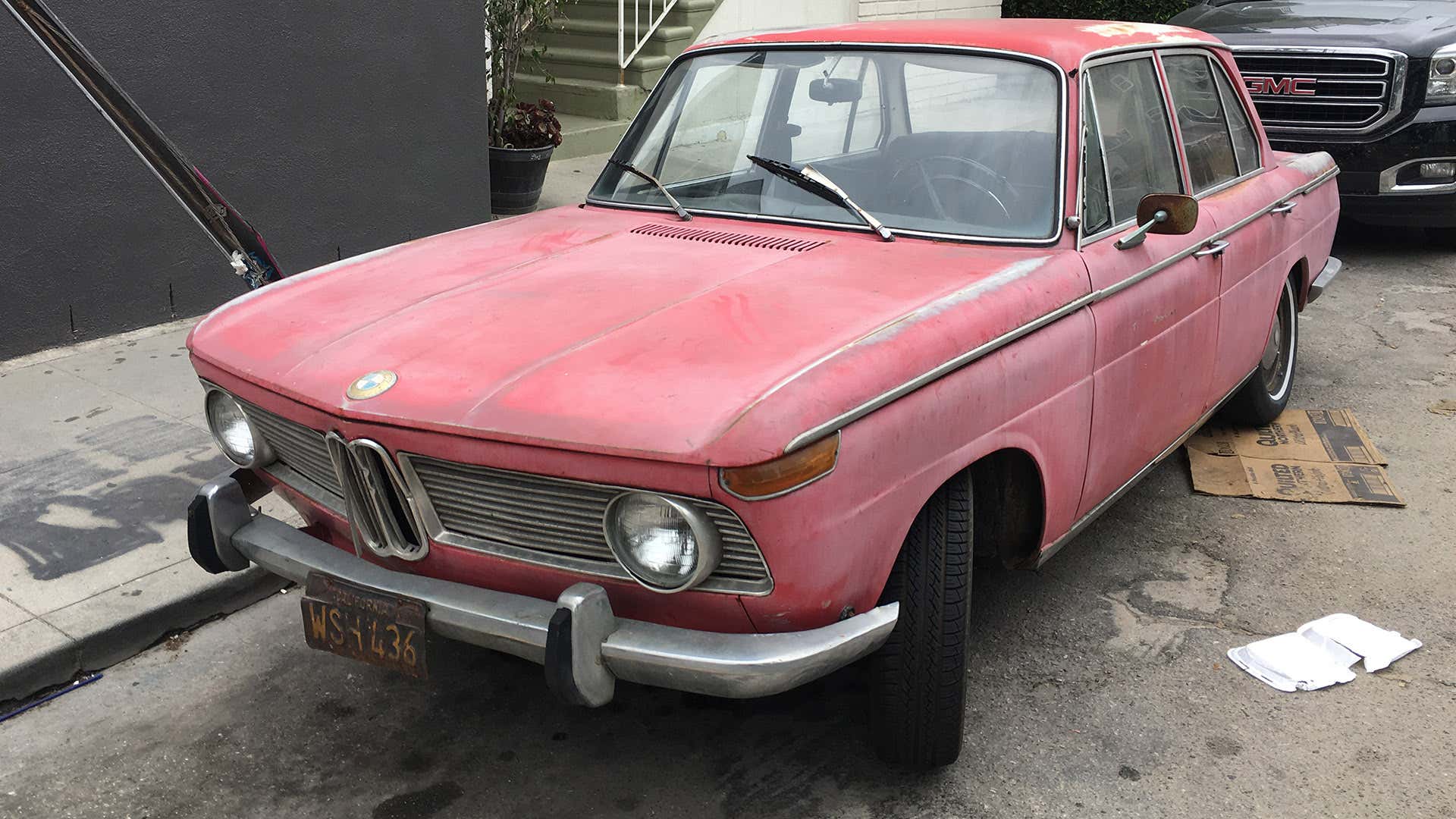 A faded red BMW parked on an LA curb. 一个褪色的红色bmw停在洛杉矶路边。