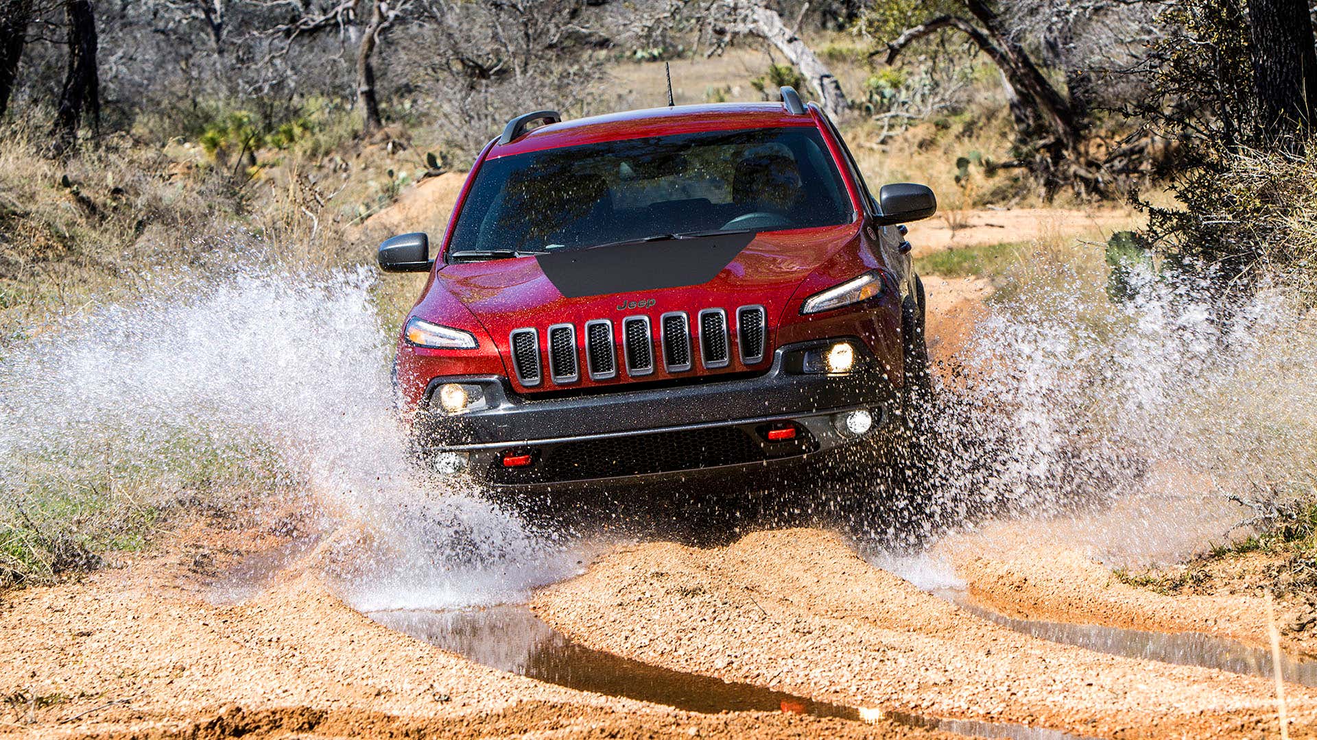 A red Jeep Cherokee splashes in the mud. 一个红色的吉普切诺基飞溅在泥里。