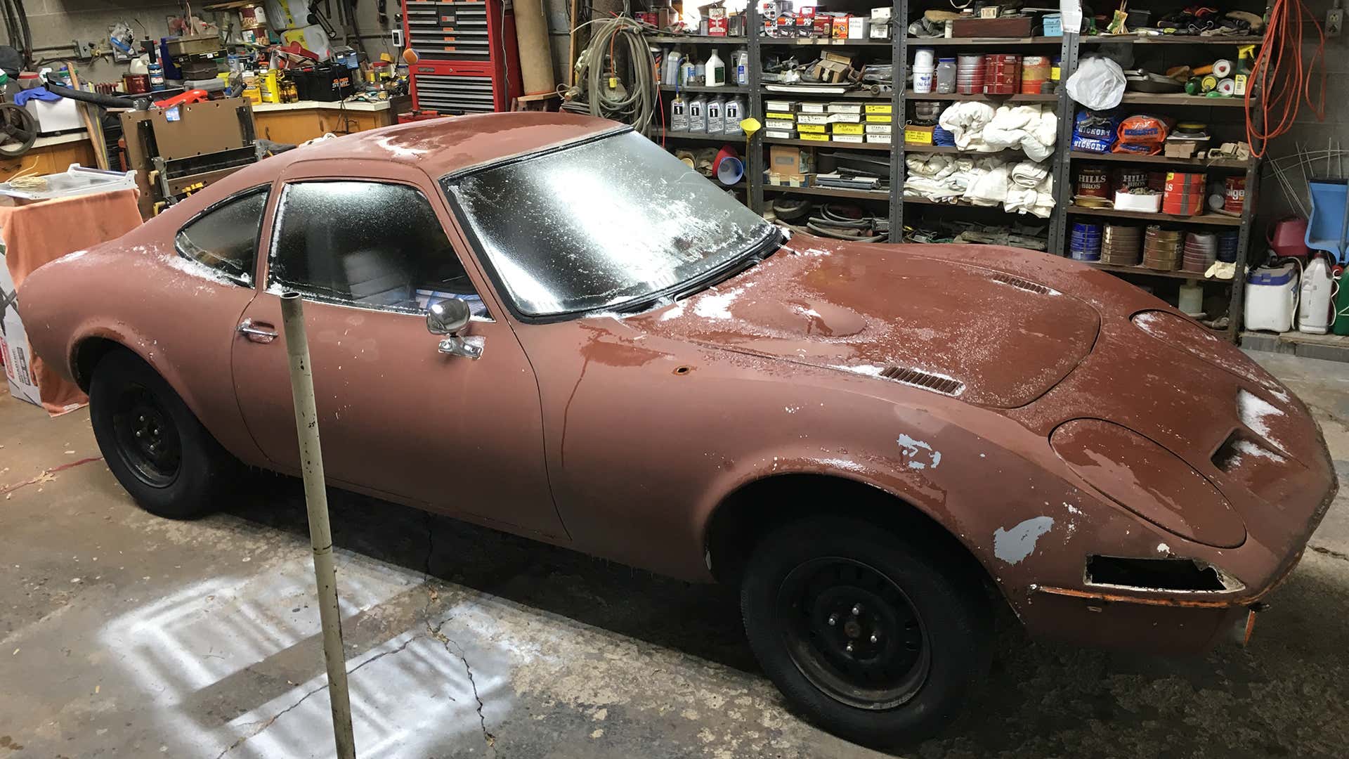 A brown Opel GT in a chaotic garage. 一辆棕色的欧宝GT在一个混乱的车库。