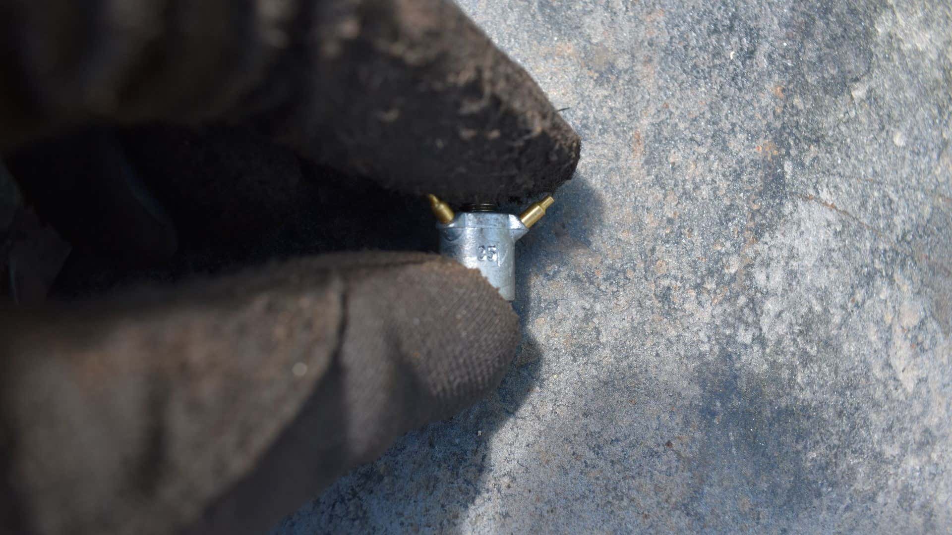 A squirter from a Holley carburetor held in place by work gloves. 由工作手套持有的霍利化油器的突口。