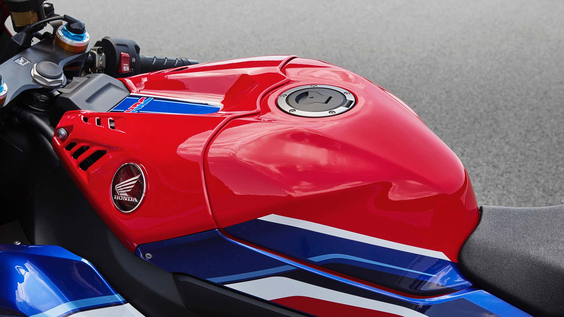 A close-up of the gas tank on a red, white, and blue Honda CBR sport bike. 红色、白色和蓝色本田CBR运动自行车上油箱的特写镜头。