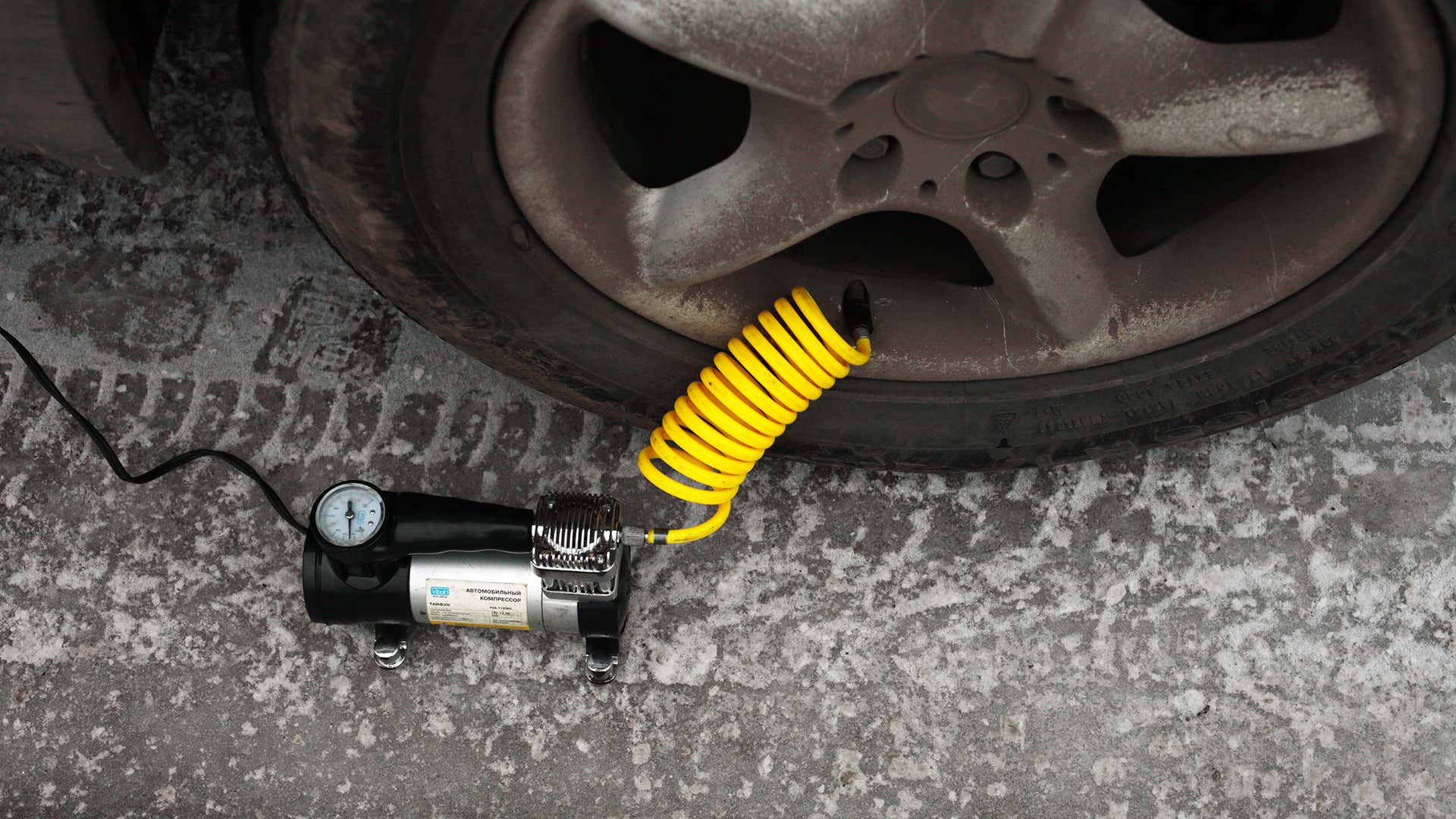 A black tire inflator with a yellow coiled hose connected to a BMW wheel and tire. 黑色轮胎打气筒,黄色软管卷连接到宝马车轮和轮胎。