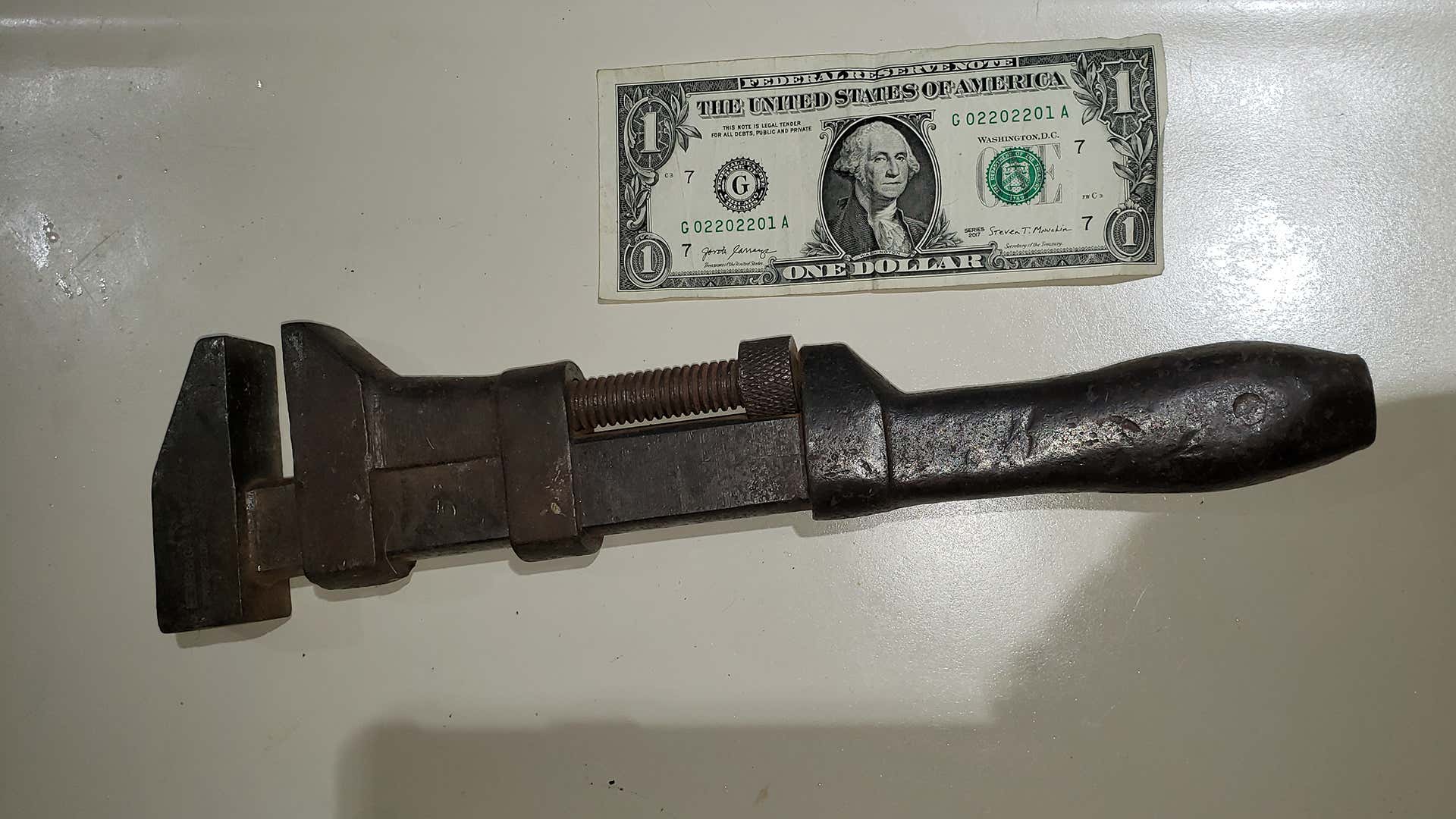 An old railroad wrench next to a dollar bill. 一张美元钞票旁边的旧铁路扳手。