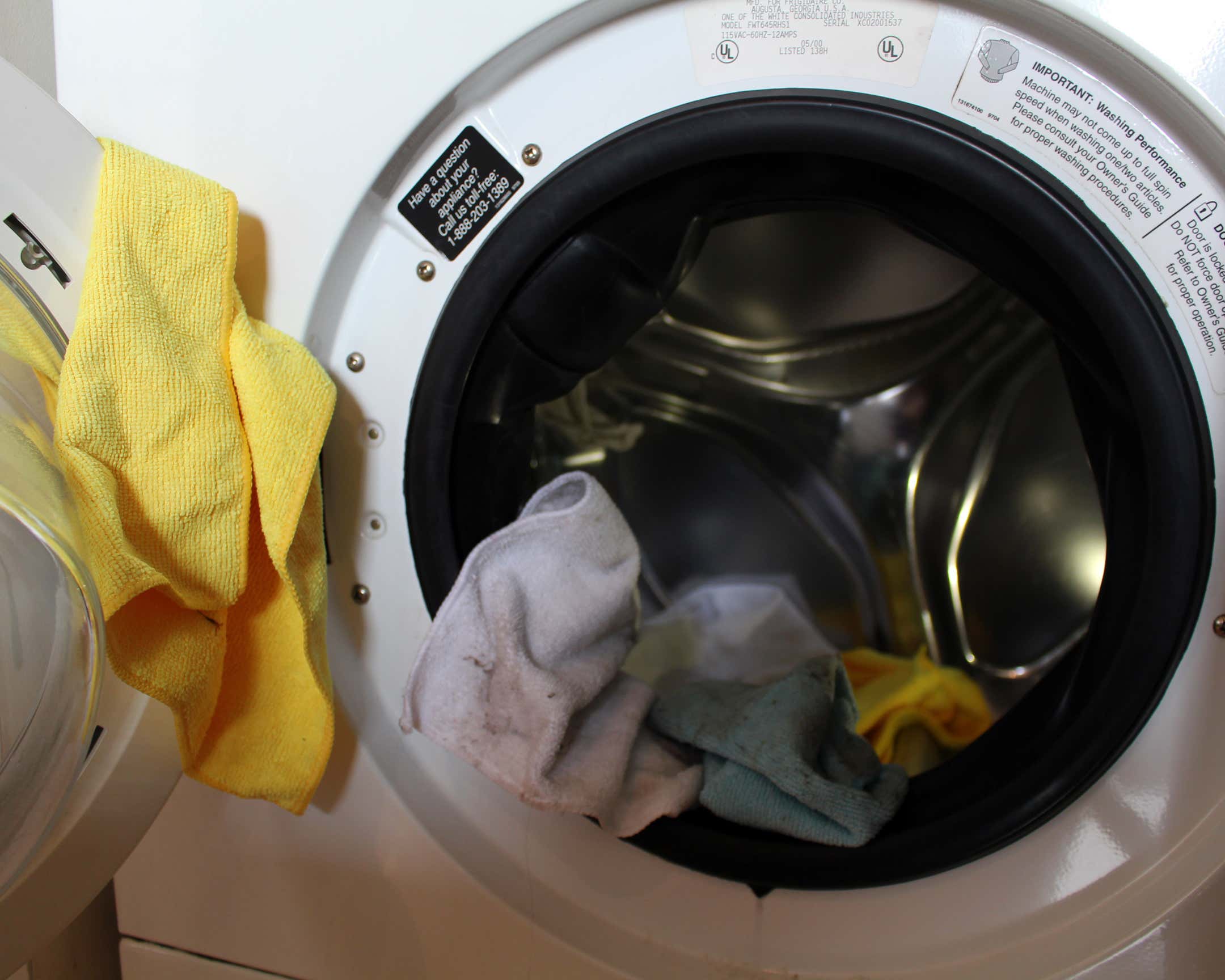 蓝色、黄色和白色的超细纤维毛巾挂在一台白色的前置洗衣机上。