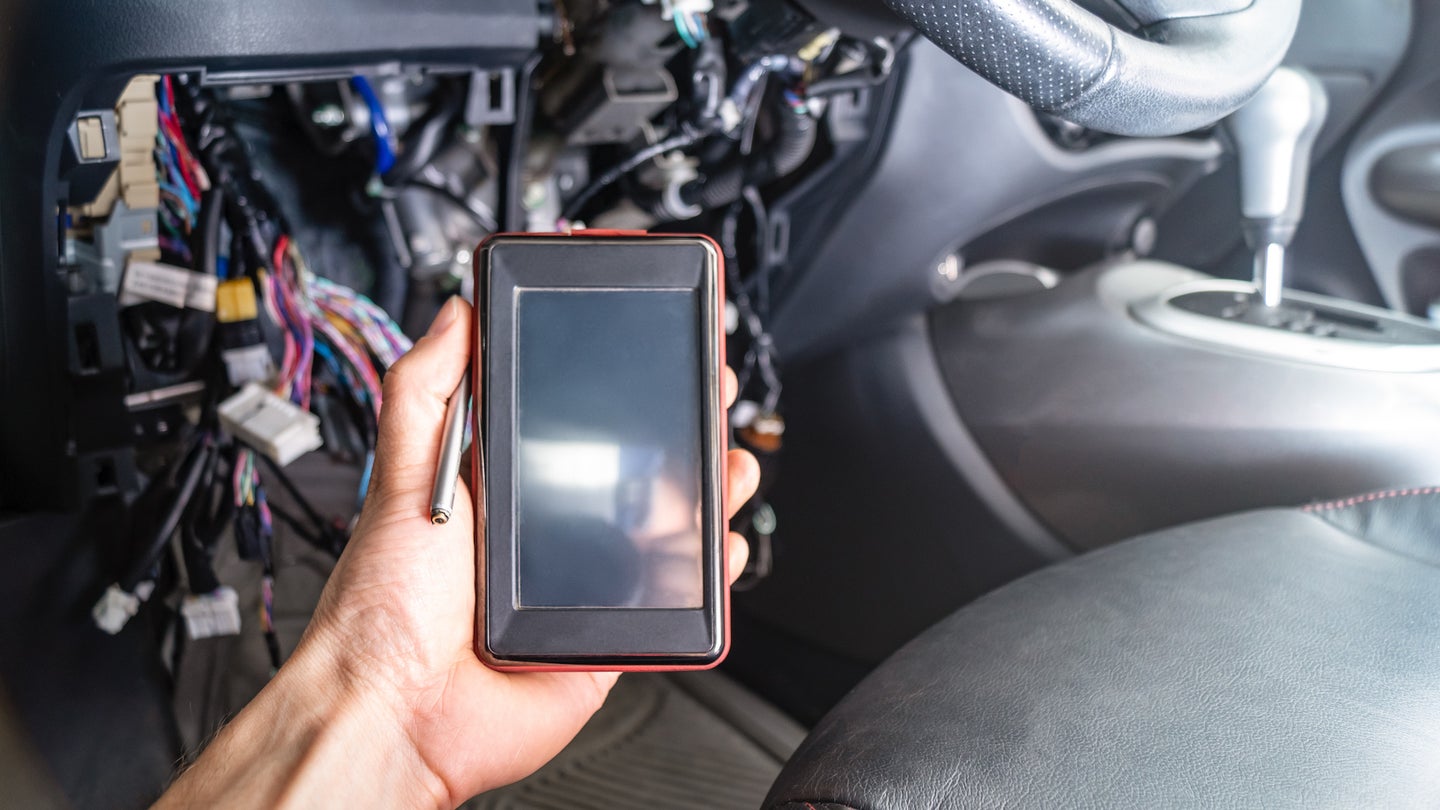 汽车故障诊断:电工手持带有OBD2接口的便携式自动扫描仪。在汽车内部的背景与拆除的面板和电线。